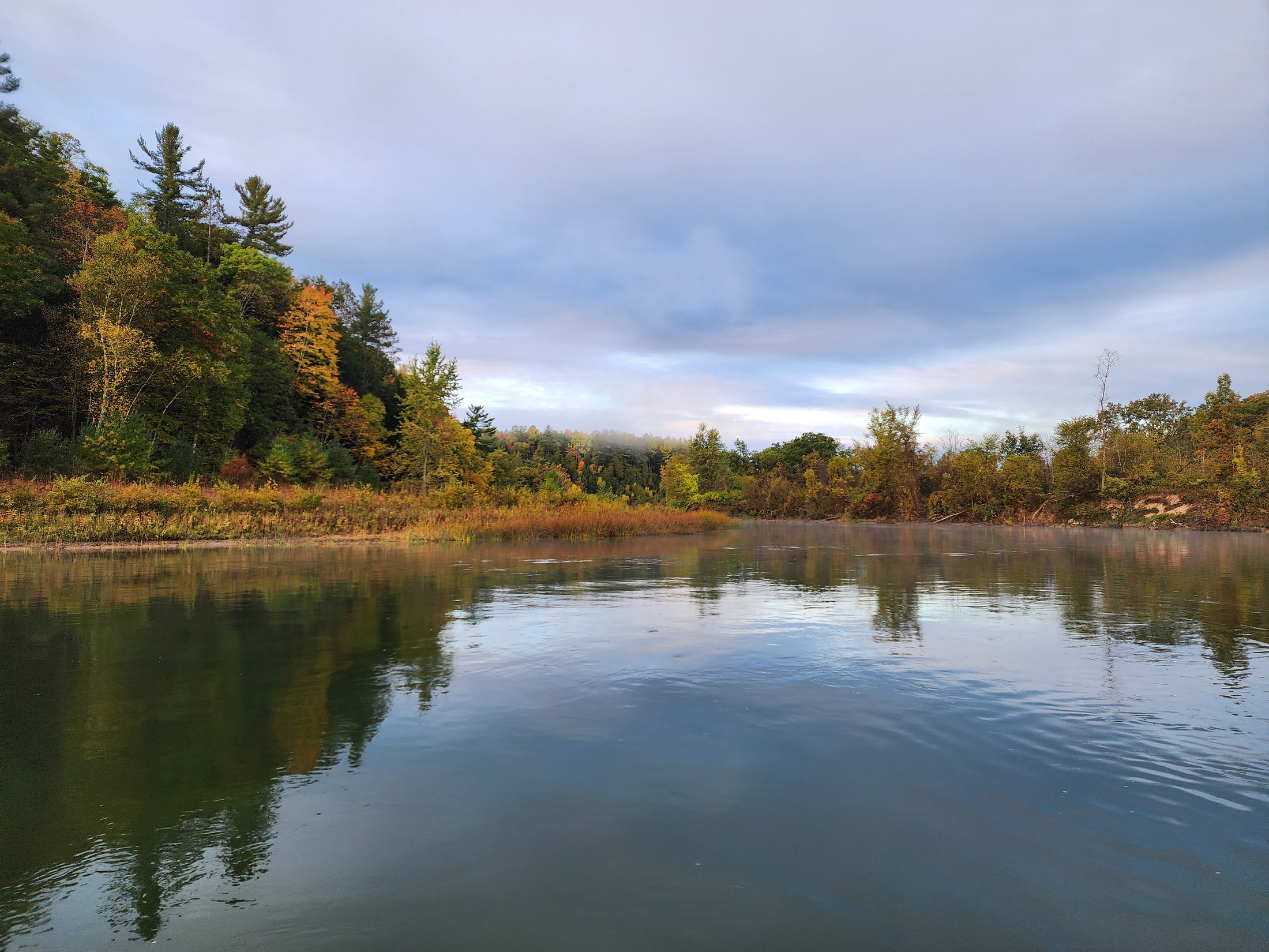 A quiet river bend reflecting autumn trees beneath an overcast sky